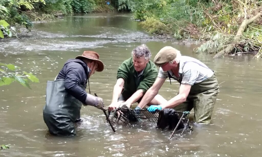 A photo of three men pulling debris from a river