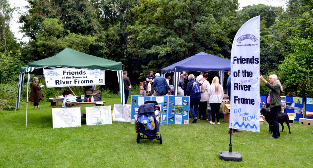 A photo of people gathered around two stalls in a meadow with information display boards. 